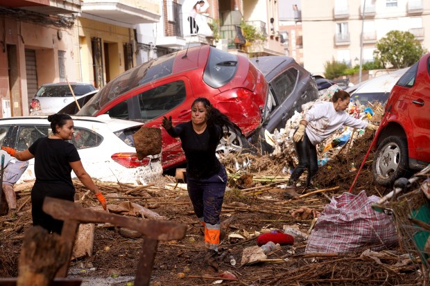 Residents clean the street next to cars piled up after being swept away by floods in Valencia, Spain, Wednesday, Oct. 30, 2024. (AP Photo/Alberto Saiz)