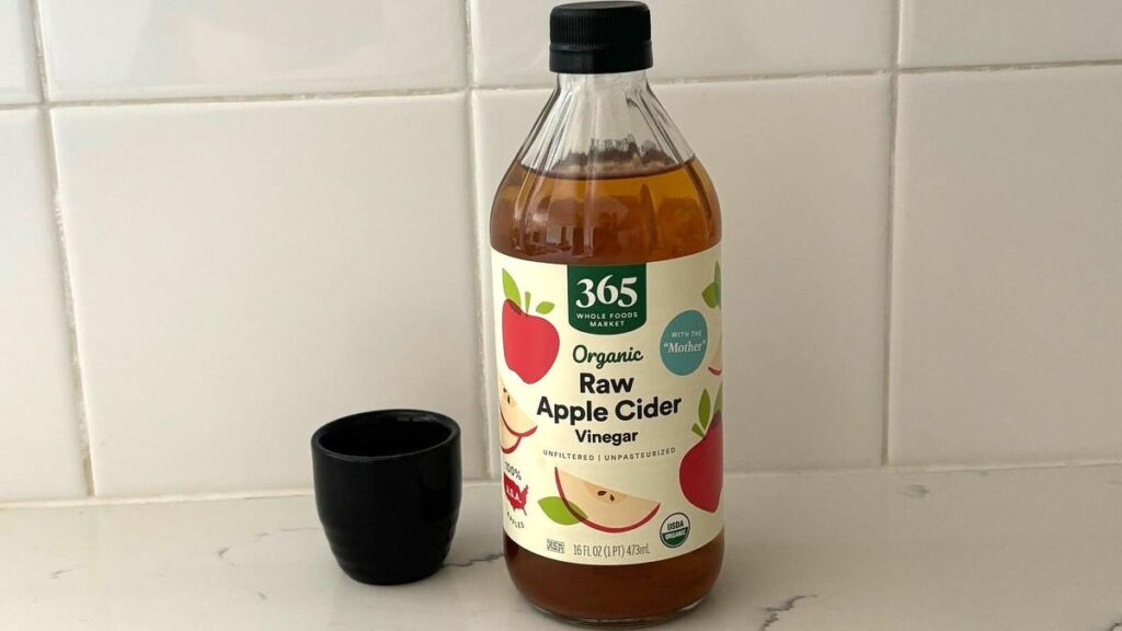 Apple Cider Vinegar for Health: Top 4 Health Benefits You Should Know About A bottle of Whole Foods 365 raw apple cider vinegar next to a tiny black vase on a marble kitchen counter.