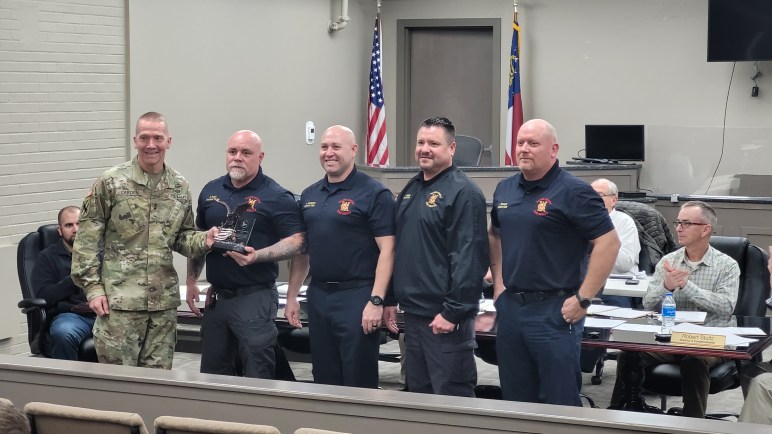 A man from the Georgia National Guard presents an award to four firefighters