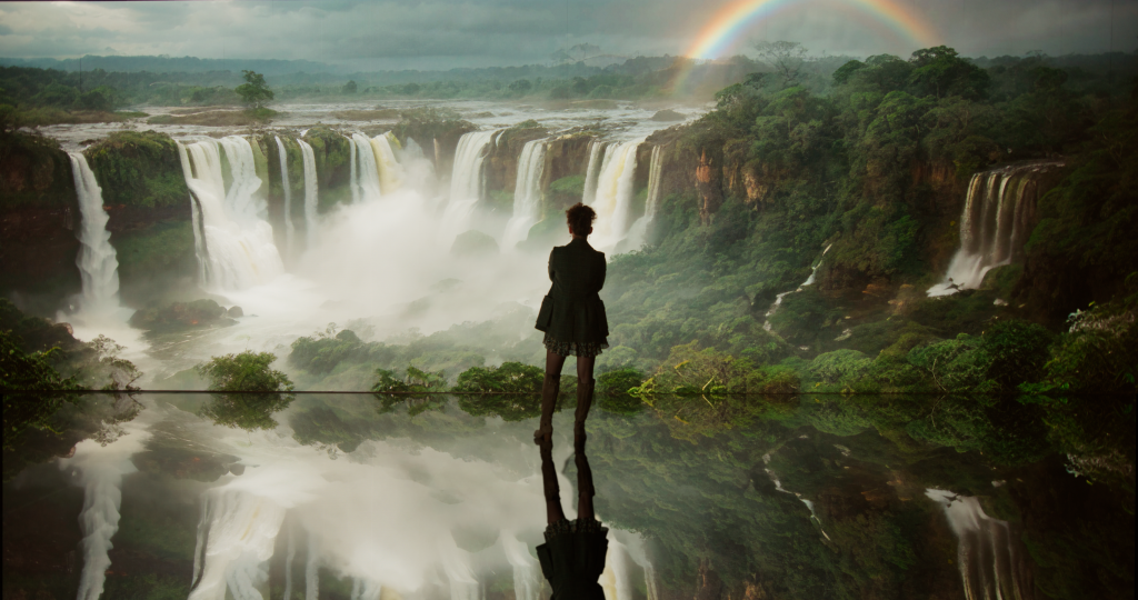 An AI-generated image of a person looking out over a giant waterfall with a rainbow