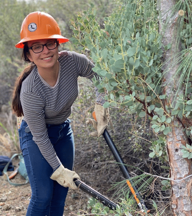 A woman wearing an orange hard hat, striped shirt and jeans woks to a repair a trail on Figuroa Mountain. (Los Padres Forest Association Inc. photo)