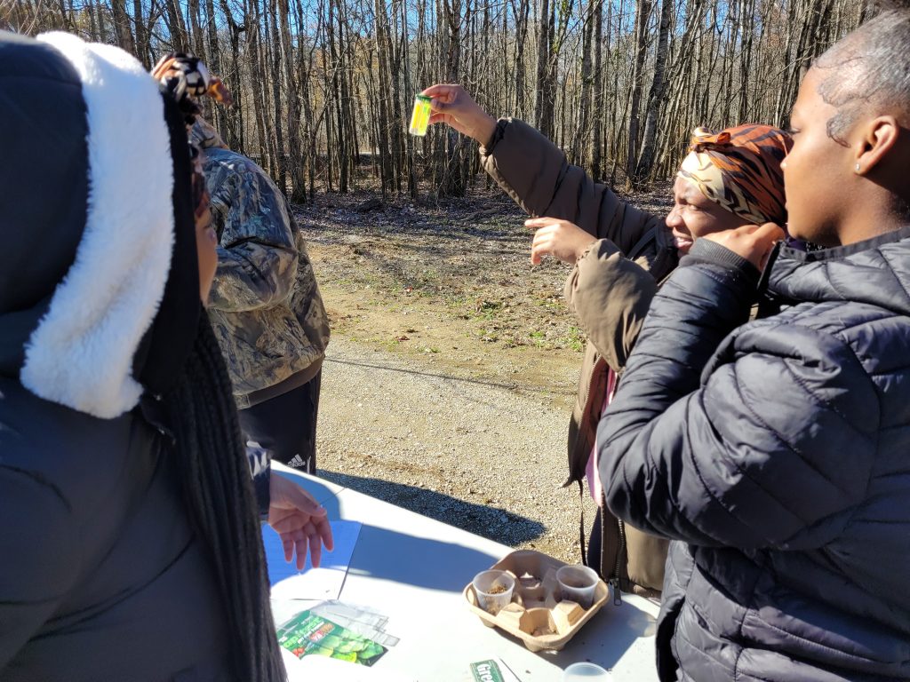 students at outdoor classroom checking water in a vial with trees in background