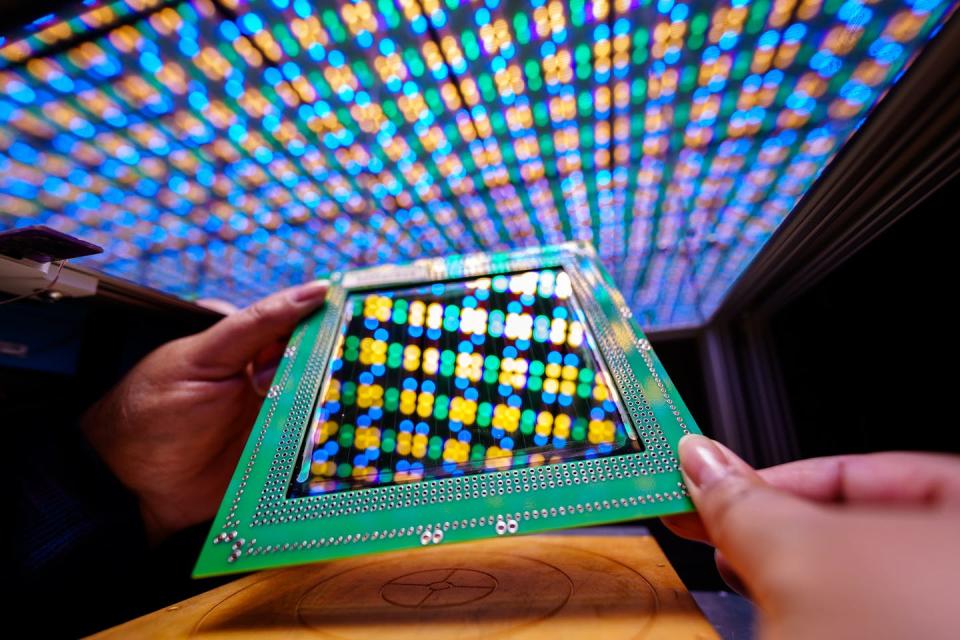 Hands hold a square photovoltaic cell reflecting colors