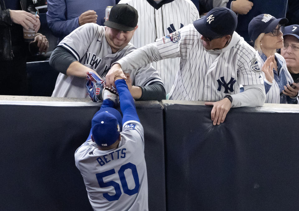 NEW YORK, NEW YORK - OCTOBER 29: Fans Austin Capobianco (L) and John Peter (R) interfere with Mookie Betts #50 of the Los Angeles Dodgers as he attempts to catch a fly ball in foul territory during the first inning of Game Four of the 2024 World Series against the New York Yankees at Yankee Stadium on October 29, 2024 in the Bronx borough of New York City. The play resulted in an out. (Photo by Al Bello/Getty Images)