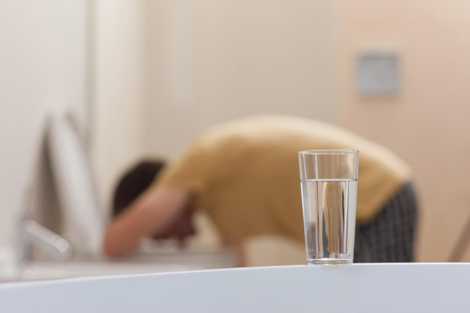 A man vomits into a toilet in the background, with a water reminding people to hydrate.