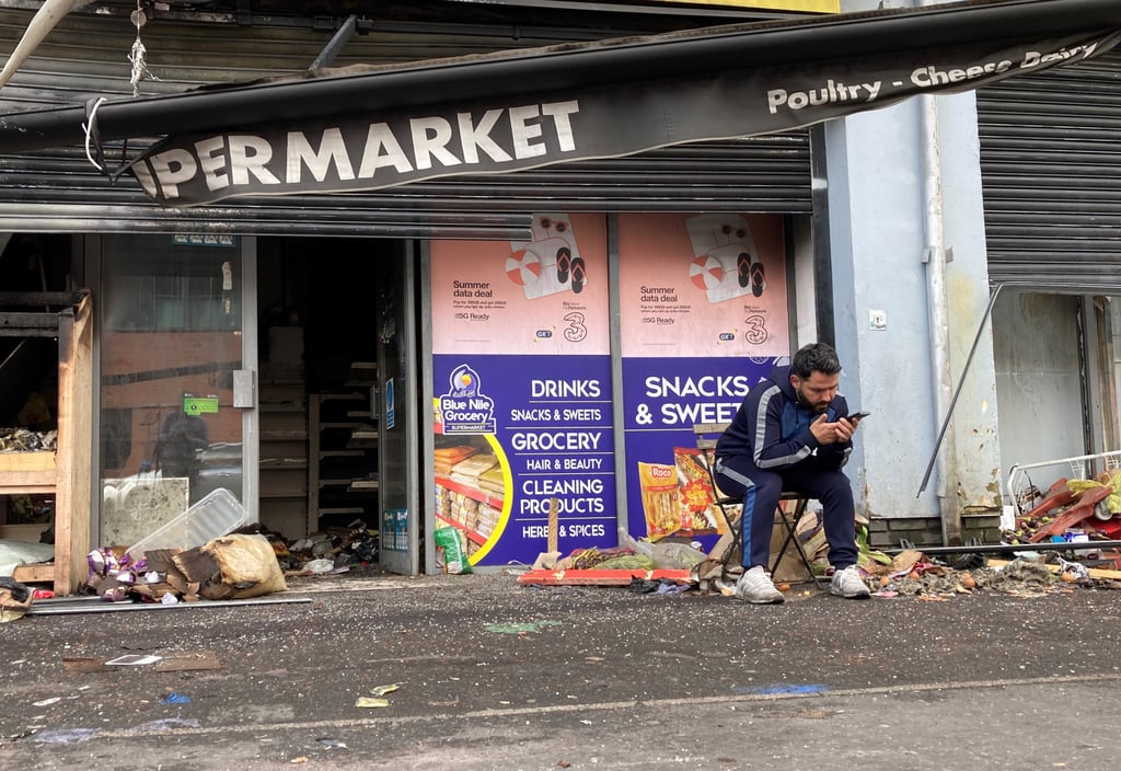 An owner of a destroyed supermarket sits outside his shop on Donegall Road in Belfast, Northern Ireland, on August 6, 2024. The shop was burned during disorder in the area following an anti-immigration protest. Photo: dpa