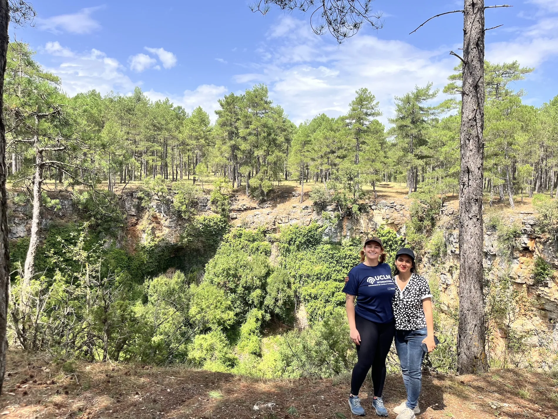 Jill Aire poses with a friend in front of a sunny forest clearing in Spain.