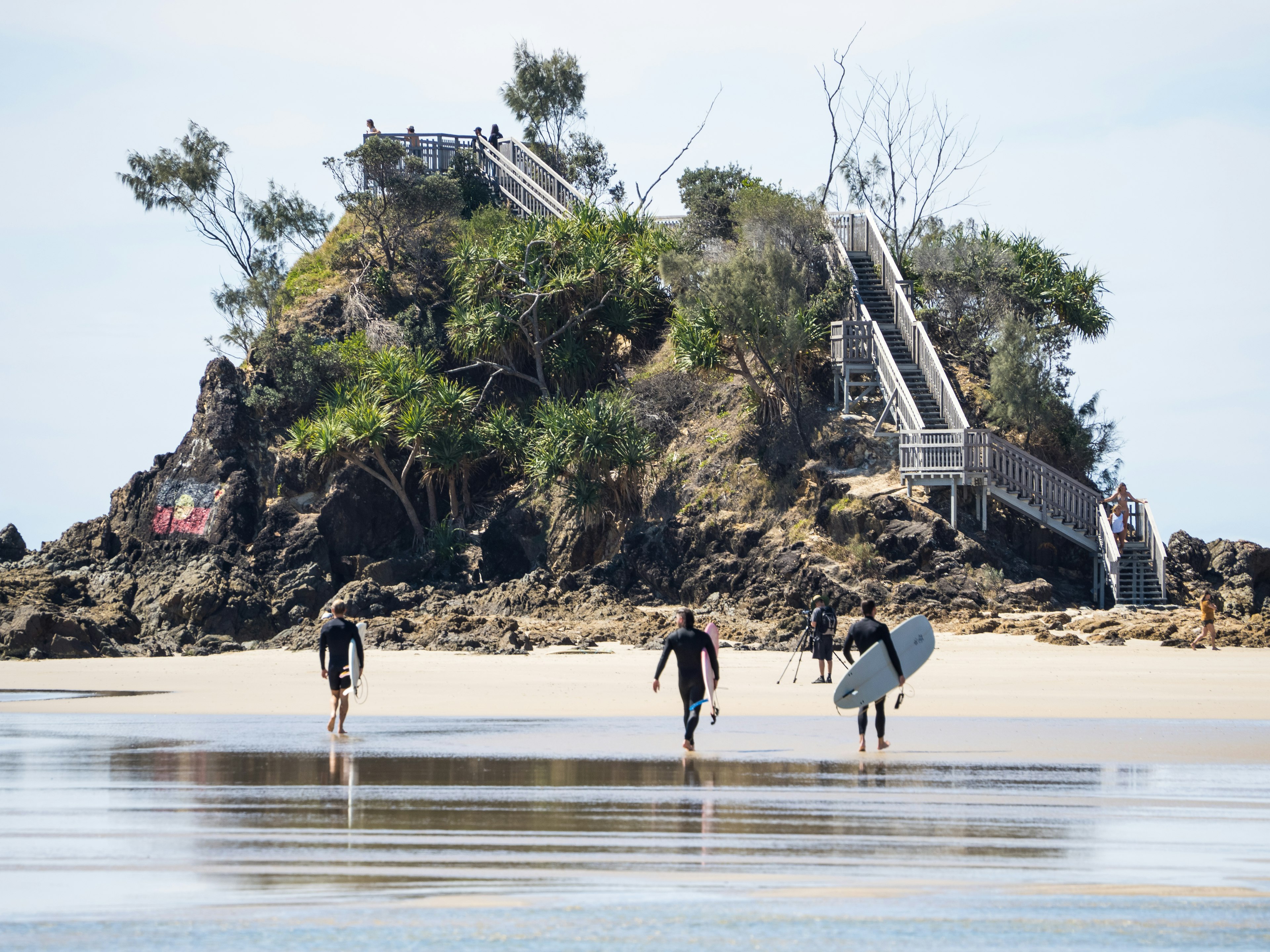 Male surfers carrying their surfboards along the beach at The Pass, Byron Bay.