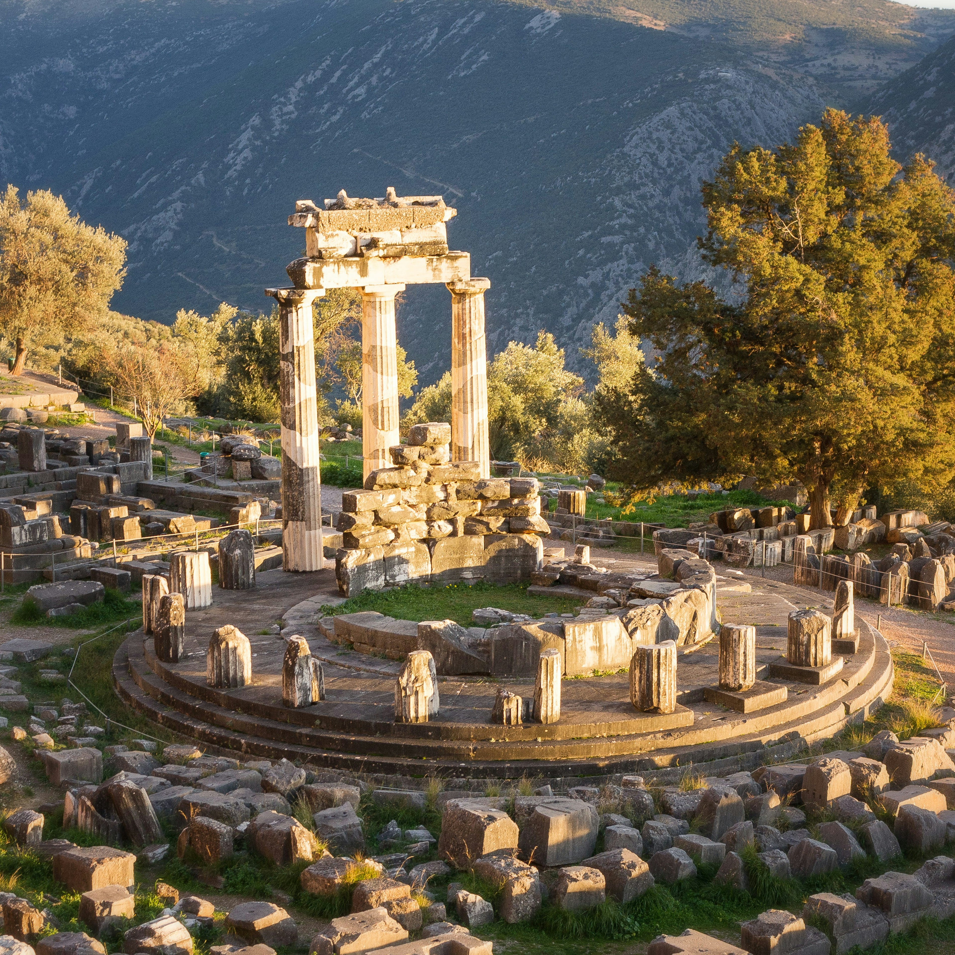 Sunlit ruins with columns in a circle at the Sanctuary of Athena at Delphi, Greece.