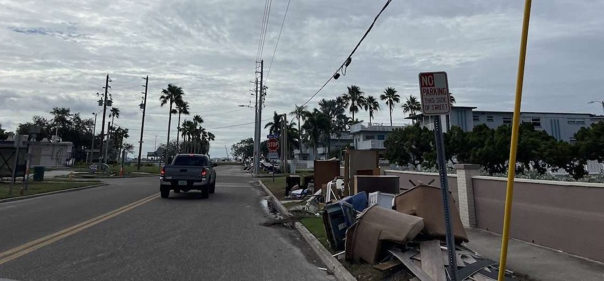 A photo of a road in Gulfport with condos on one side and homes on the other with debris lining the sidewalk.