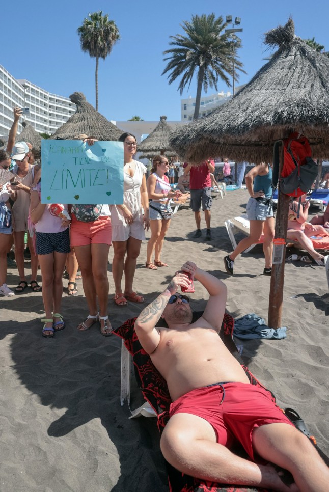 A protester holds a sign reading "The Canary Islands have a limit" as thousands march on Las Americas beach during a demonstration to protest against mass tourism, in Arona on the Spanish Canary island of Tenerife, on October 20, 2024. Thousands of flag-waving demonstrators hit the streets across Spain's Canary Islands today to demand changes to the model of mass tourism they say is overwhelming the Atlantic archipelago. Rallying under the slogan "The Canary Islands have a limit", demonstrators waving white, blue and yellow flags of the Canary Islands, marched by tourists sitting in outdoor terraces in Playa de las America before they rallied on the beach chanting "This beach is ours" as tourists sitting on sunbeds under parasol shades looked on. (Photo by DESIREE MARTIN / AFP) (Photo by DESIREE MARTIN/AFP via Getty Images)