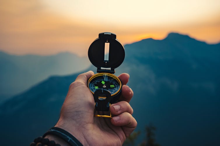 close up of hand holding compass, mountains in background