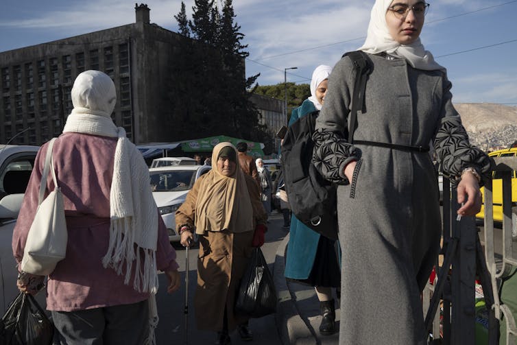 Women in niqabs walk on a city street.