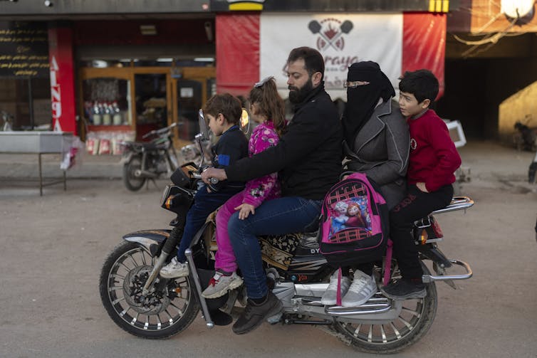 A man drives a motorbike with a woman in a burka and three young children.