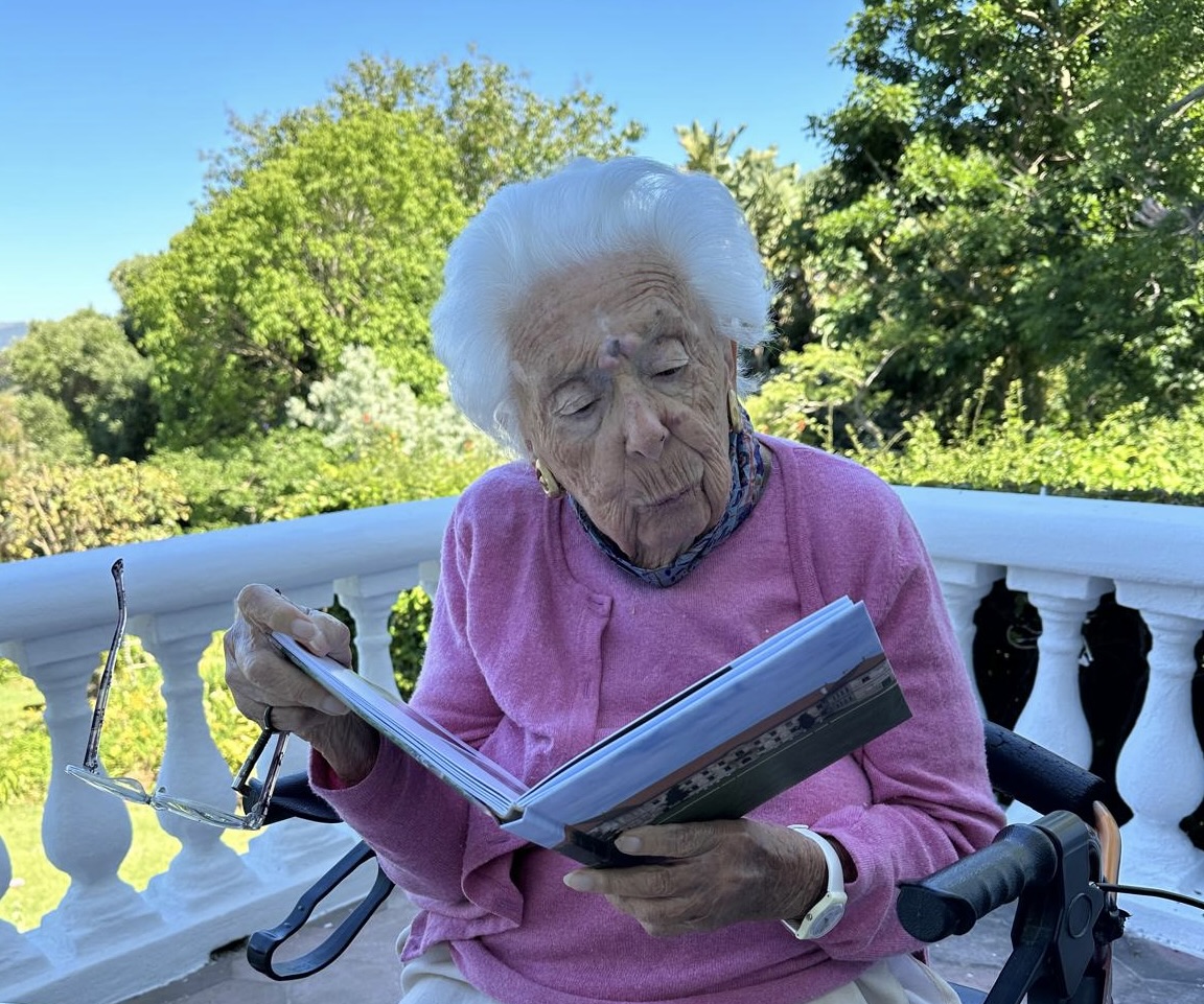Elderly woman reading a book outdoors.