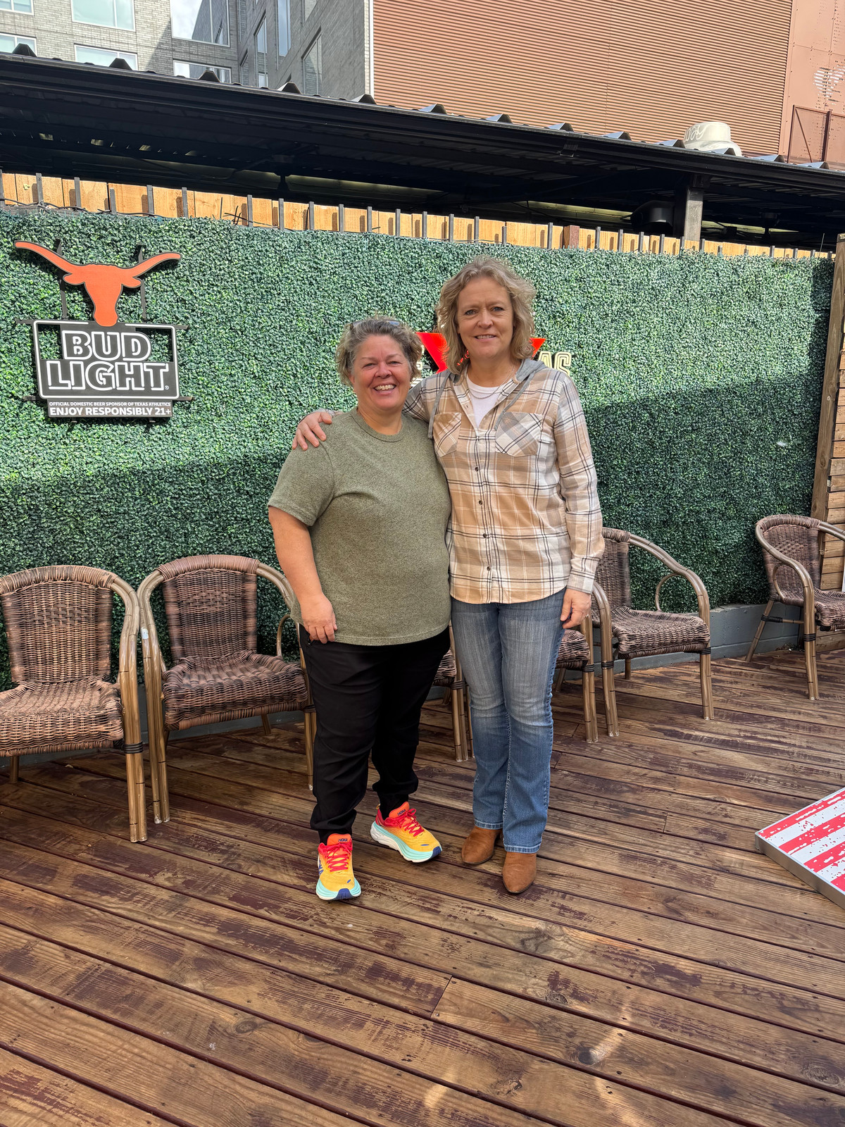 Two women stand together with their arms around each other on the patio of a sports bar.