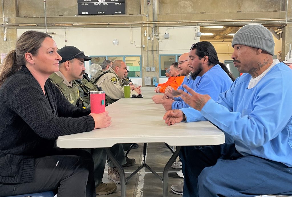 Staff members on the left and incarcerated people on the right while all seated at a long table for a CCI town hall.