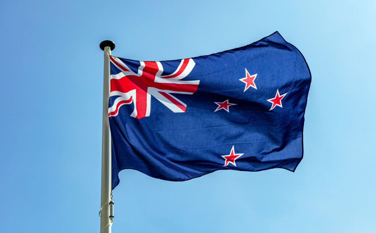 New Zealand flag, New Zealand national symbol waving against clear blue sky, sunny day