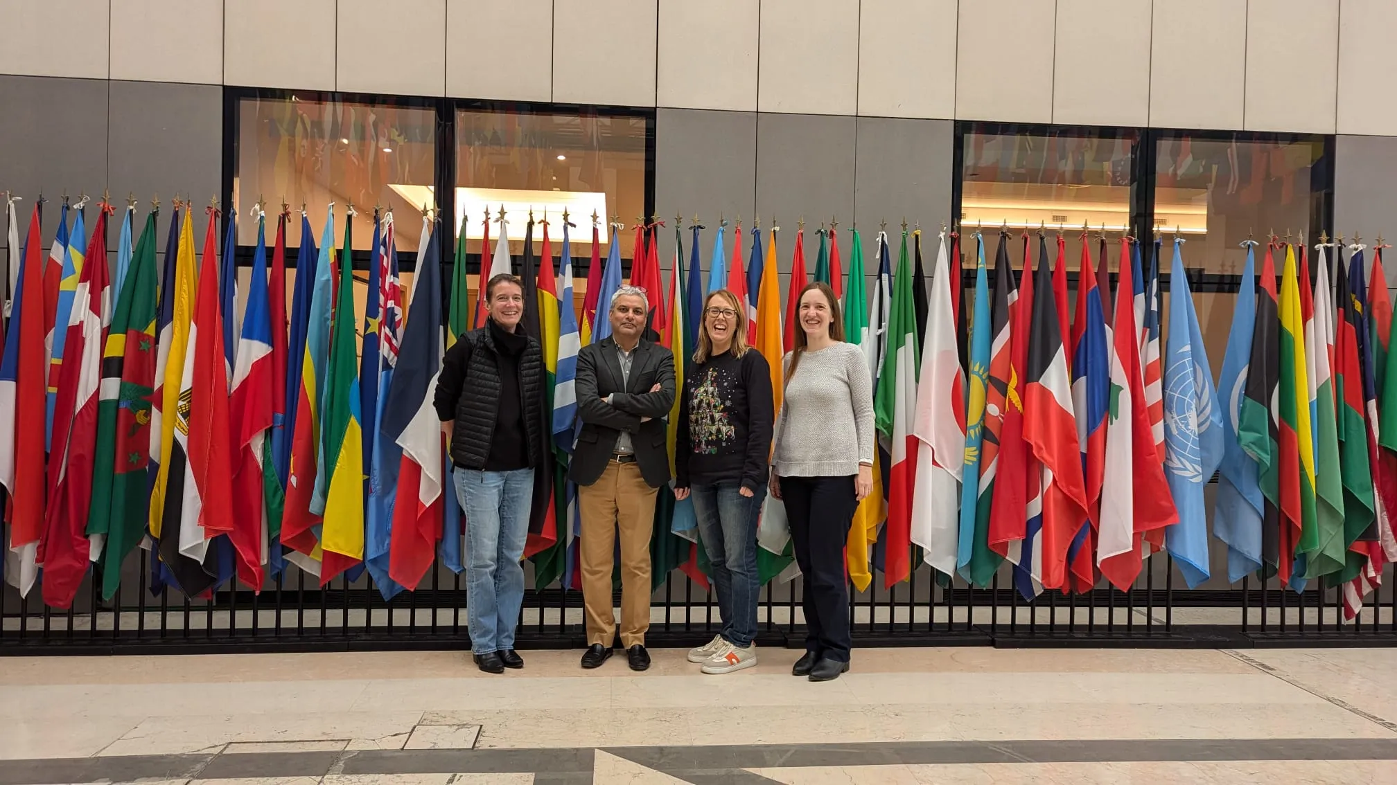 Rajat Panwar standing with two colleagues in front of a row of flags from around the world.