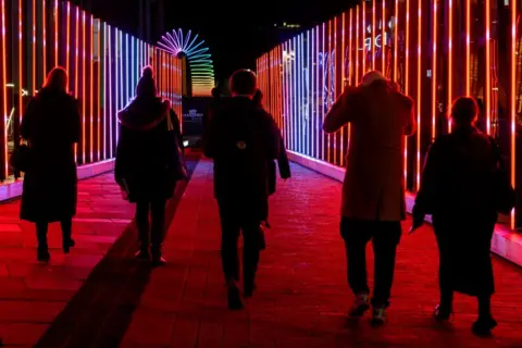 Ian Georgeson Five people walking through a bright installation.