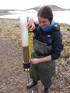 a woman stands on rocky ground with a tube half-filled with sediment