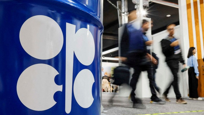 People walk past an installation depicting barrel of oil with the logo of Organization of the Petroleum Exporting Countries