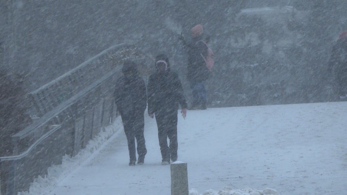 Two people wearing winter jackets and bundled for the cold walk across a snow footbridge. 