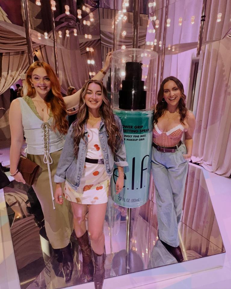 Three women posing with a large bottle of e.l.f. setting spray.