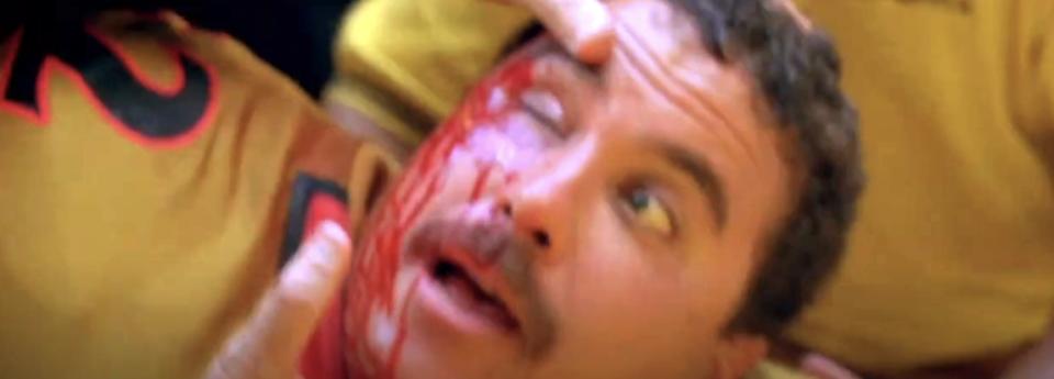 A man with a surprised expression has red liquid on his face, lying down