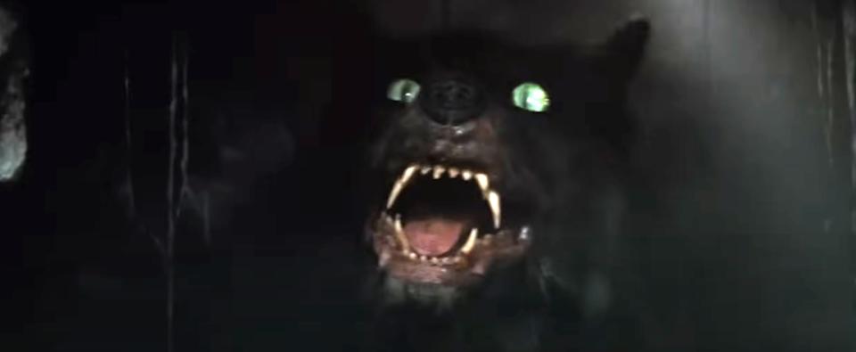 A menacing werewolf with glowing eyes and sharp teeth emerges from the darkness, snarling