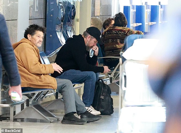The actor took a seat to check his phone as he waited to board his flight