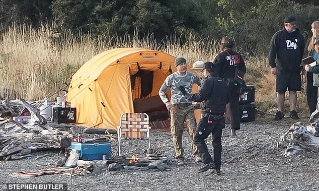 The actor wore cargo pants and a camouflage-print top as he stood near a fire pit and bright yellow tent