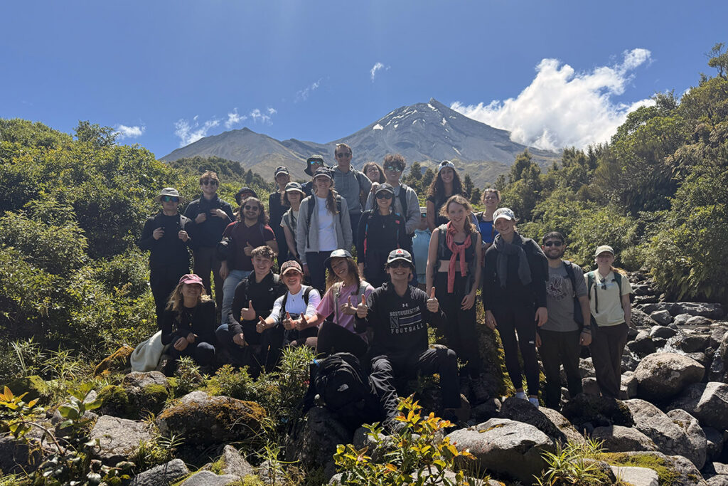 Students listen to their professor outside of a scenic view of New Zealand