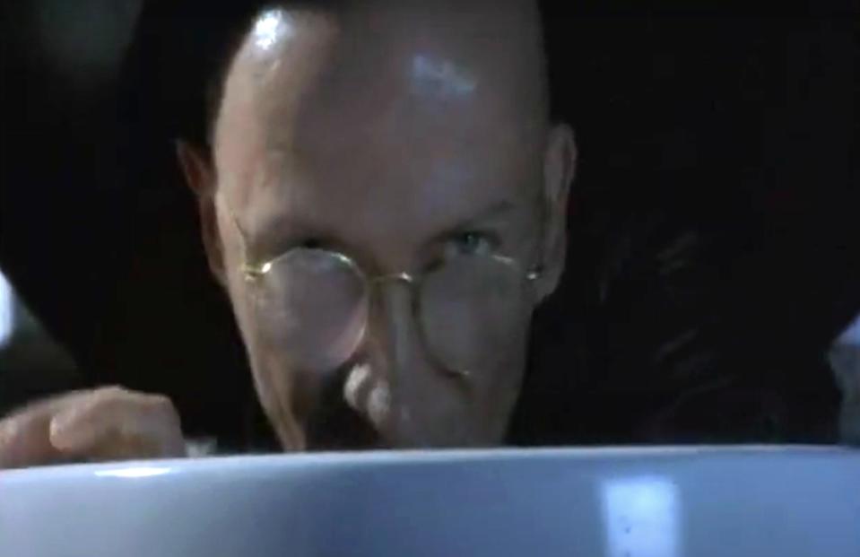 A bald man with glasses leans over a bowl, creating an intense and suspenseful scene