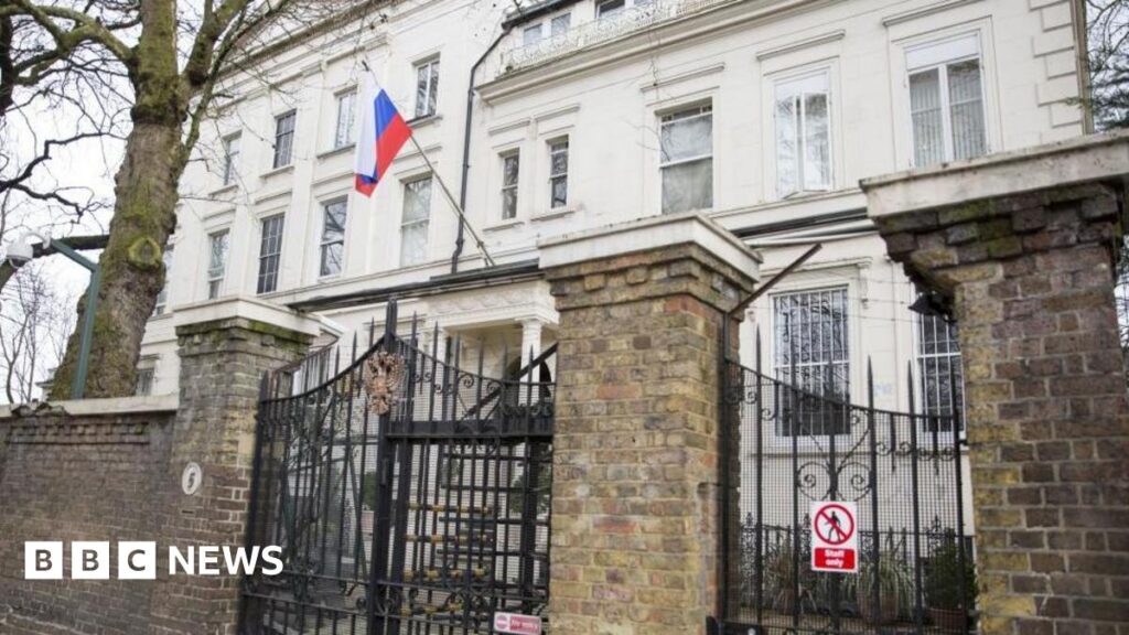 External image of the Russian embassy building in London - a white building behind a stone fence with large black wired gate.