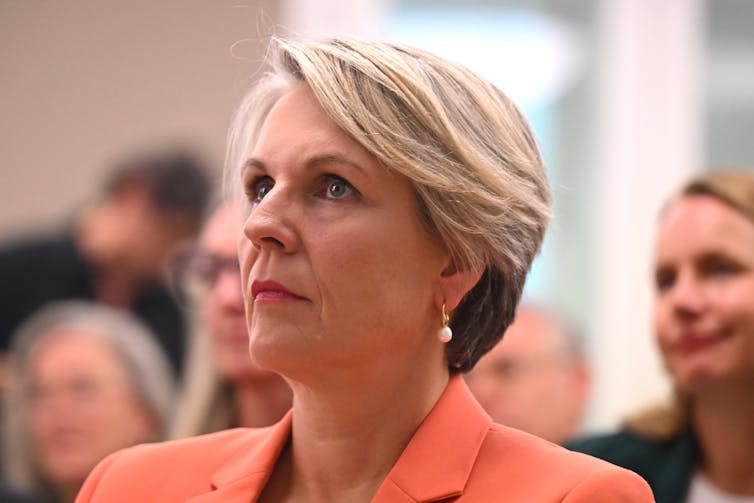 blonde woman in orange jacket looks serious