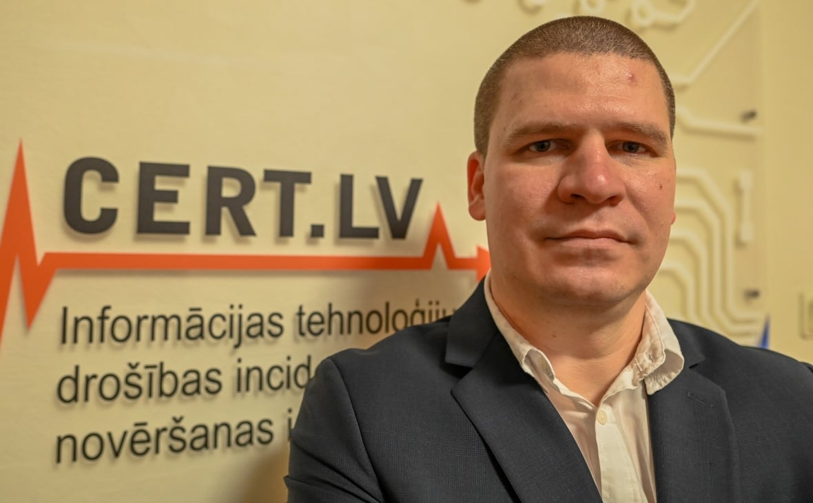 A man stands in front of a sign in Latvian 
