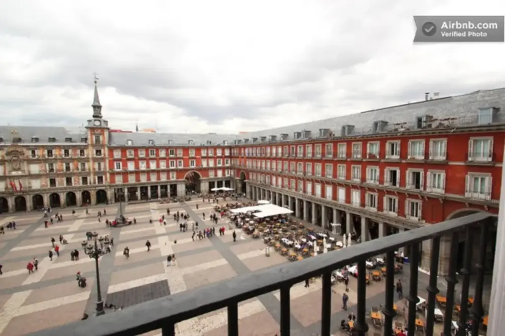 Spain Targets Illegal Rentals in Madrid A view of Madrid’s Plaza Mayor from the balcony of an Airbnb apartment, overlooking the historic square and its surrounding buildings.