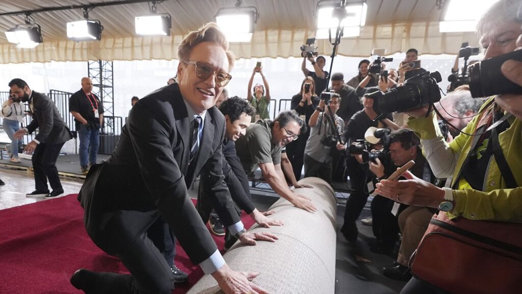 Conan O'Brien, host of Sunday's 97th Academy Awards, helps to roll out the red carpet for the show at the Dolby Theatre on Wednesday, Feb. 26, 2025, in Los Angeles. (AP Photo/Chris Pizzello)