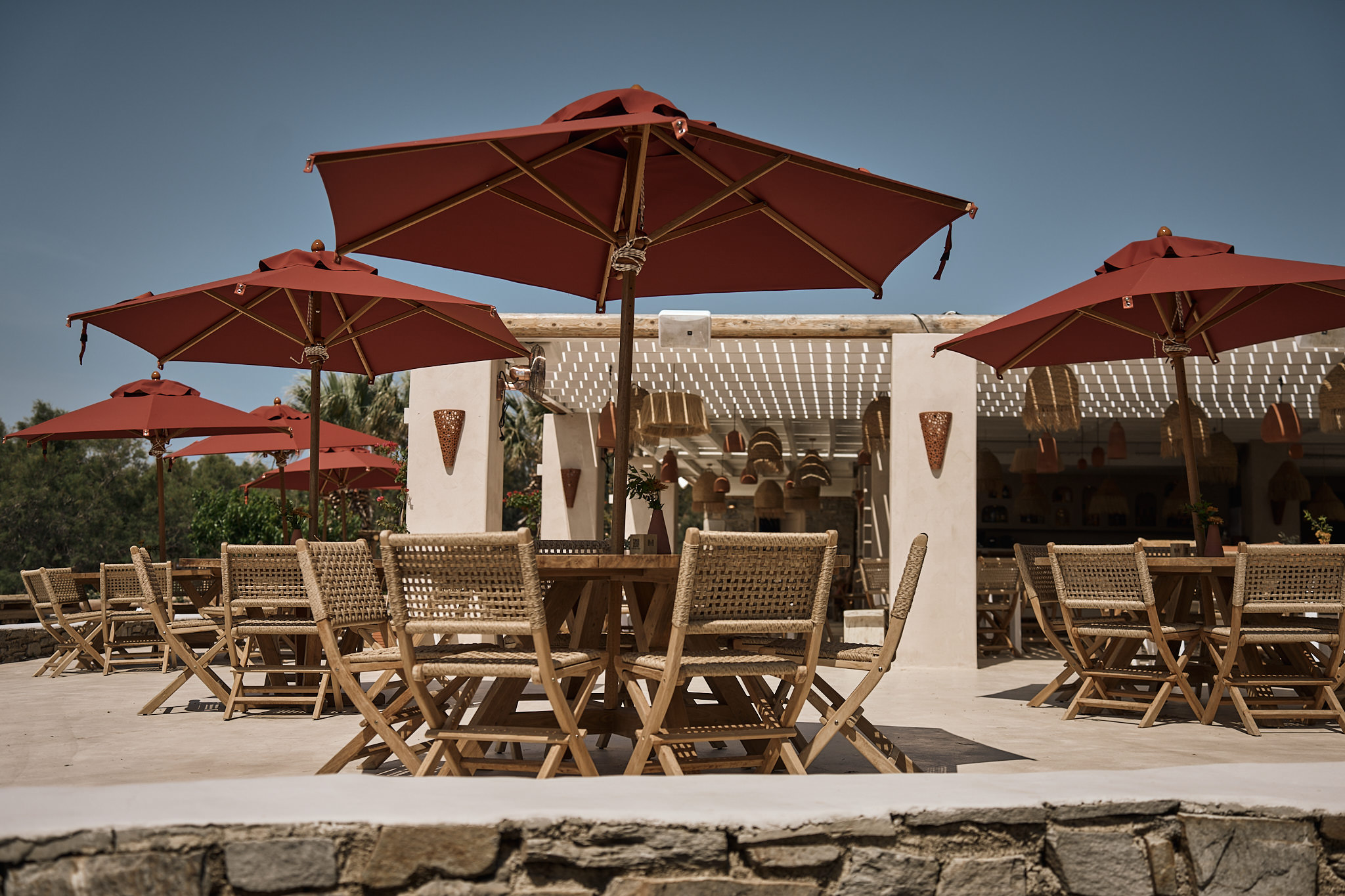 Outdoor patio seating with red umbrellas and woven chairs.