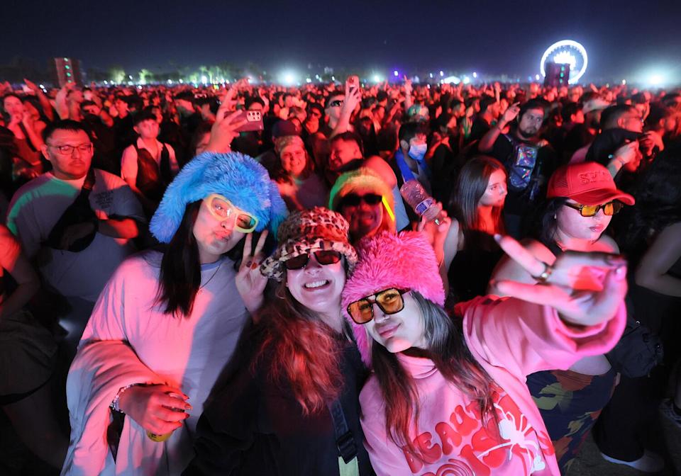 Three people pose for the camera, wear festive hats, in the middle of the crowd.