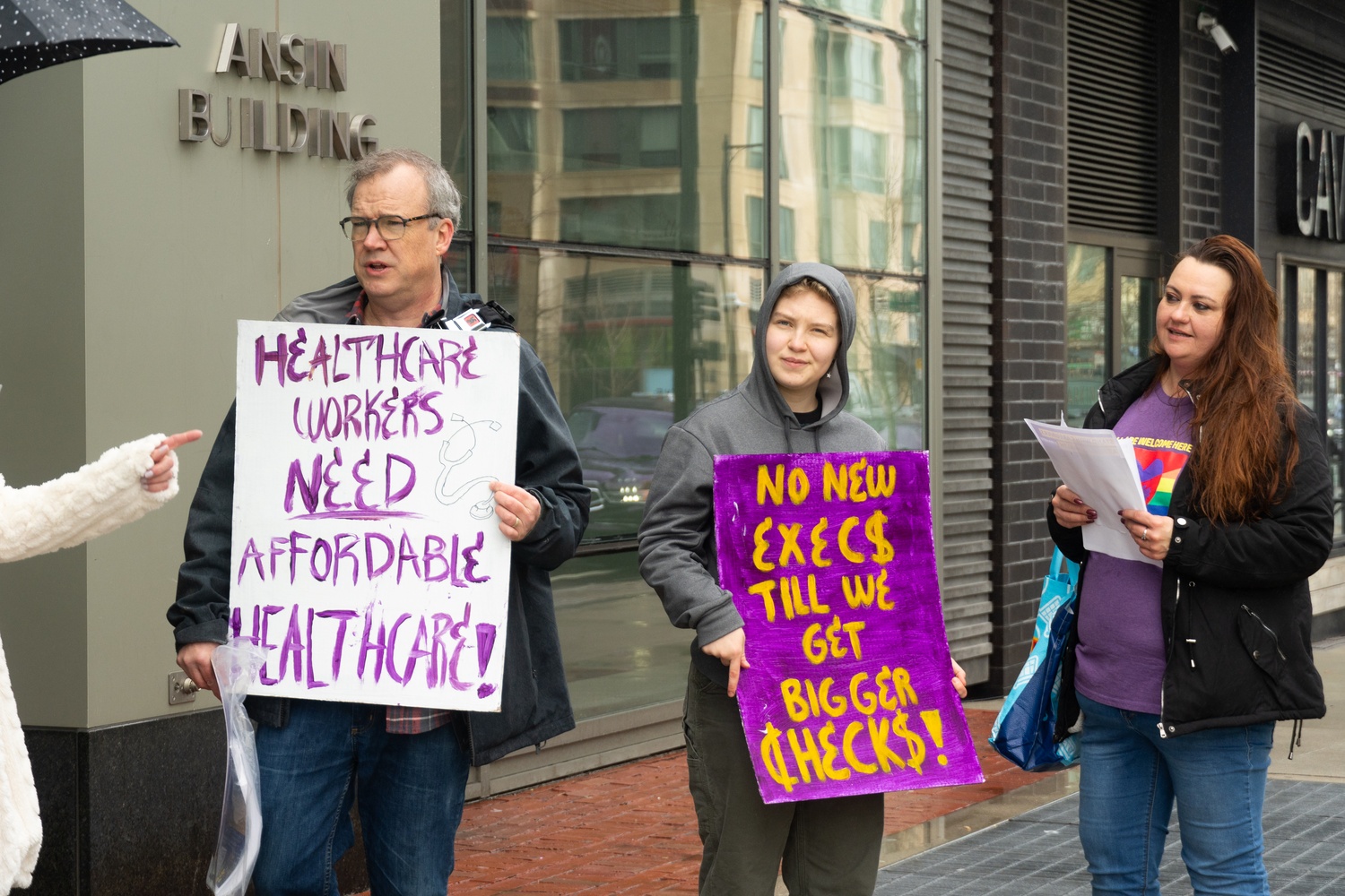 Members of Fenway Health United hold signs at the Thursday rally. They read: "No new exec$ till we get bigger check$!" and "Healthcare workers need affordable healthcare!"