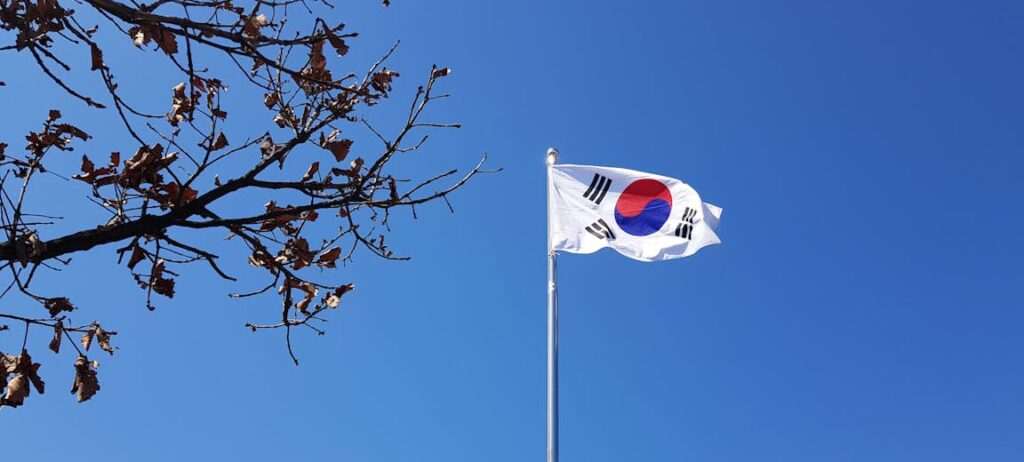 opportunities for cooperation with the EU and Spain’ South Korean flag waving on a flagpole in Yongin-si, Gyeonggi-do, with a clear blue sky and autumn tree branches in the foreground. Korea