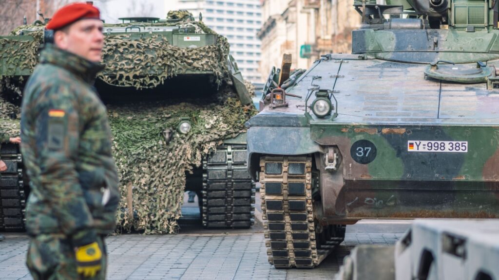 German Military Deploys to Lithuania for the First Time Since WWII German army, NATO response force or North Atlantic Treaty Organization armored crawler tanks and other military vehicles on the road of the city with soldiers.
