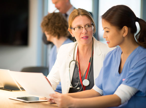Become a Master in Health Care Systems — Master’s in Health Informatics Webinar Two health care professionals review documents together at a desk in a medical office.