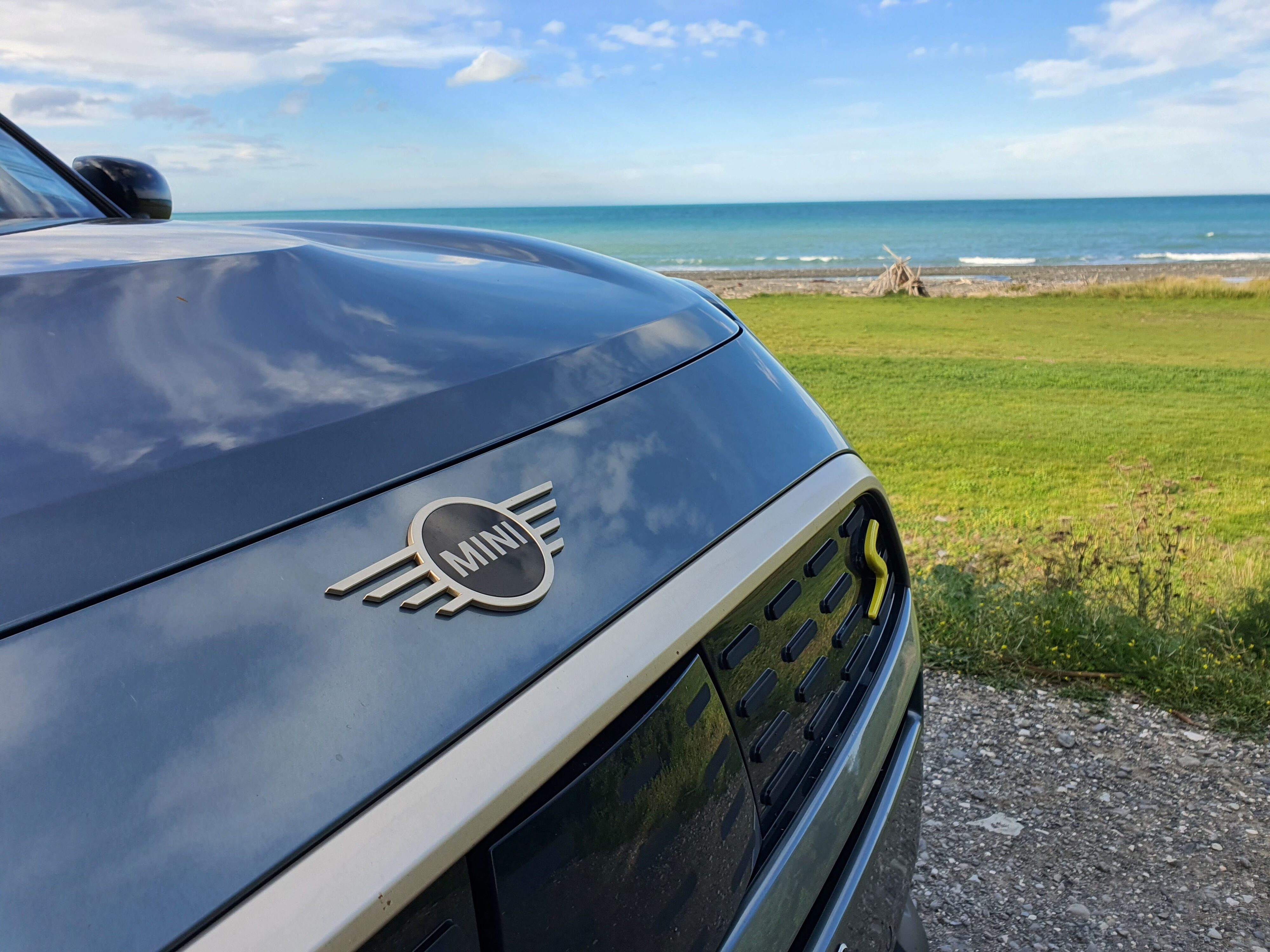 A photo of the Mini logo and green S badge on the nose of a 2025 Countryman SE All4 with the ocean in the background en route to Kaikoura.