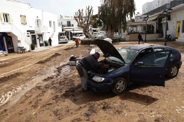 A man tries to fix a car after a powerful storm which has triggered widespread flooding at the port of Naousa, on the Aegean Sea island of Paros, Greece, Tuesday, April 1, 2025. (John Liakos/InTime News via AP)