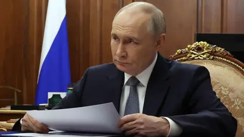 Vyacheslav PROKOFYEV/POOL/ AFP Russia's Vladimir Putin sits at a desk holding a piece of paper