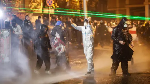 EPA Protesters wearing rain jackets and hoods are pummelled with jets of water, as one of them swears at police with hand gesture.