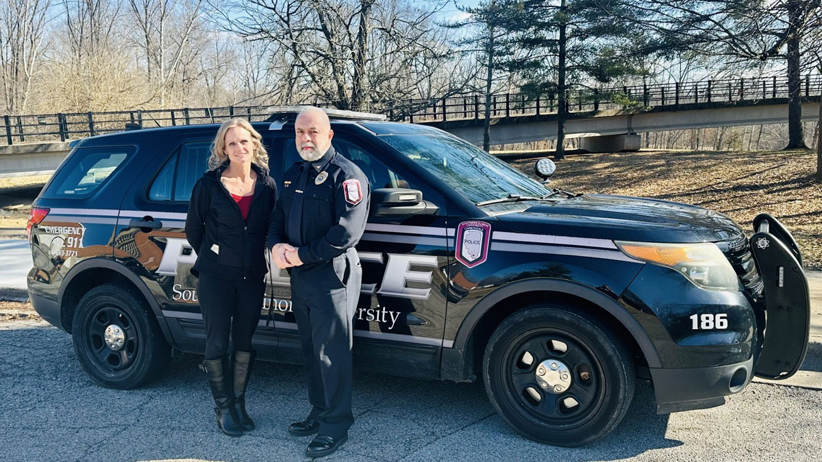 A man and woman pose for a picture next to a police car.